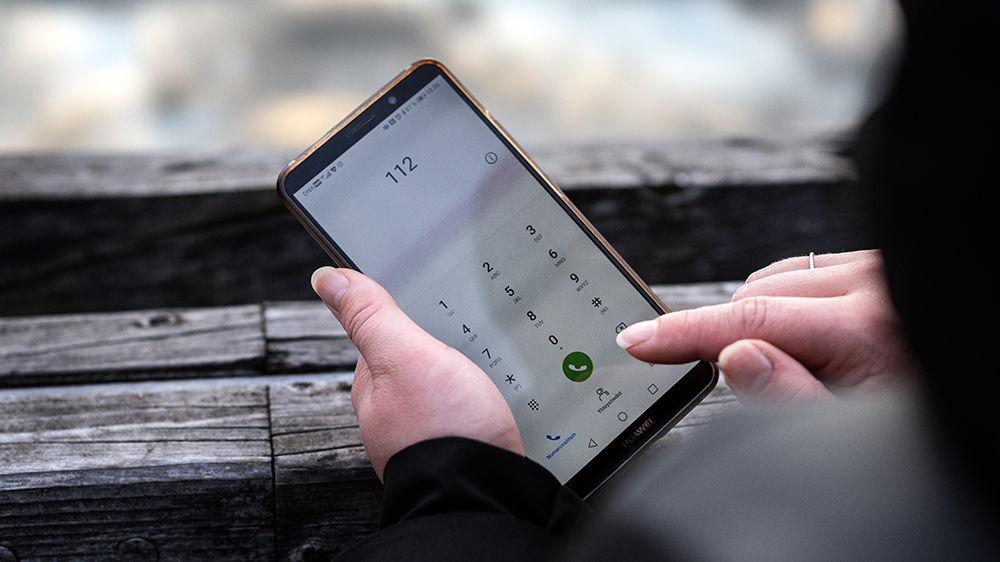 Puhelin, johon on näppäilty numero 112. Henkilö pitää puhelinta kädessään.