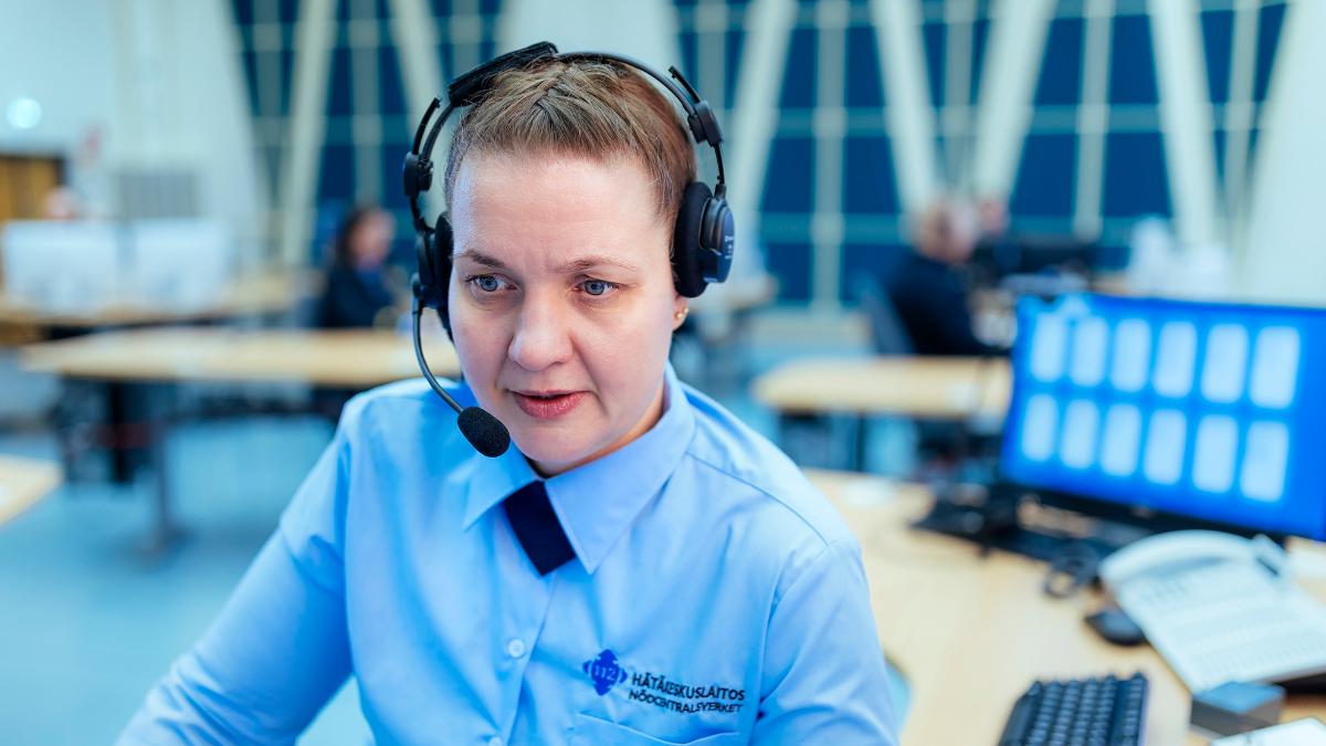 A woman in Emergency Response Centre Agency's uniform with headphones on at a computer.