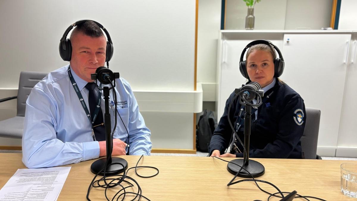 Juha Suominen ja Laura Kuurne istuvat vierekkäin pöydän ääressä. Heillä on päässään kuulokkeet ja edessään mikrofoni.