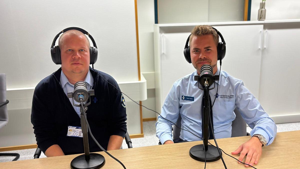 Jonne Joukanen ja Patrick Tiainen istuvat pöydän ääressä luurit päässään. Heidän edessään on mikrofonit. Miehet ovat pukeutuneet Hätäkeskuslaitoksen virkavaatteisiin.