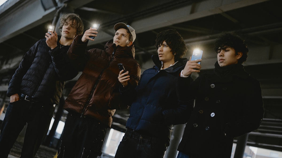 Neljä nuorta miestä seisovat rinnakkain ja kuvaavat puhelimilla.